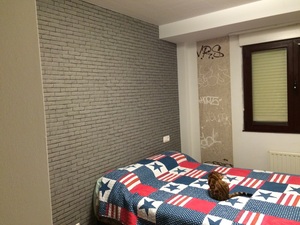 Habitación juvenil con papel pintado imitando adoquín gris.